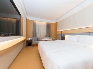 A hotel room with a large bed, a desk with a chair, a small table, and a TV. - Ji Hotel (Hefei)