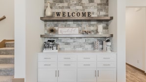 A modern entryway with a stone wall, a 'WELCOME' sign, a 'It's the most wonderful time of the year' sign, and a white console with drawers and cabinets. - Entertainment District -Walk to Stadiums - Near Six Flags -Sleeps 8 (Arlington)