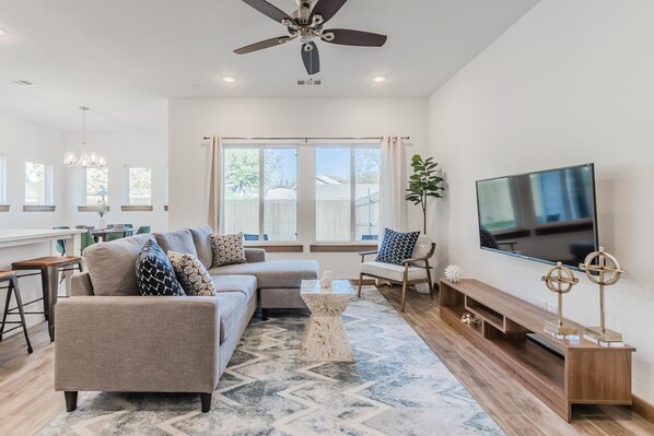 A spacious living room with a sofa set, a coffee table, a TV, and a ceiling fan. - Entertainment District -Walk to Stadiums - Near Six Flags -Sleeps 8 (Arlington)