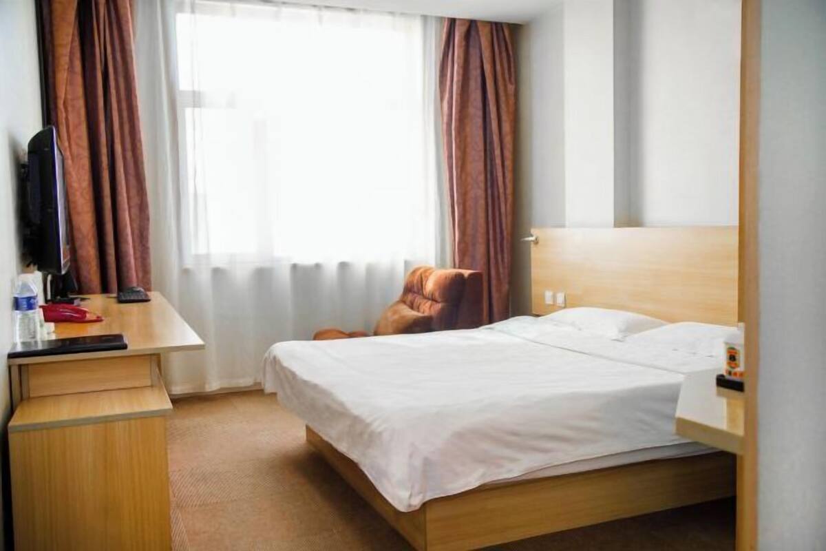 Ein Hotelzimmer mit Bett, Schreibtisch, Stuhl und einem Fenster mit Vorhängen.