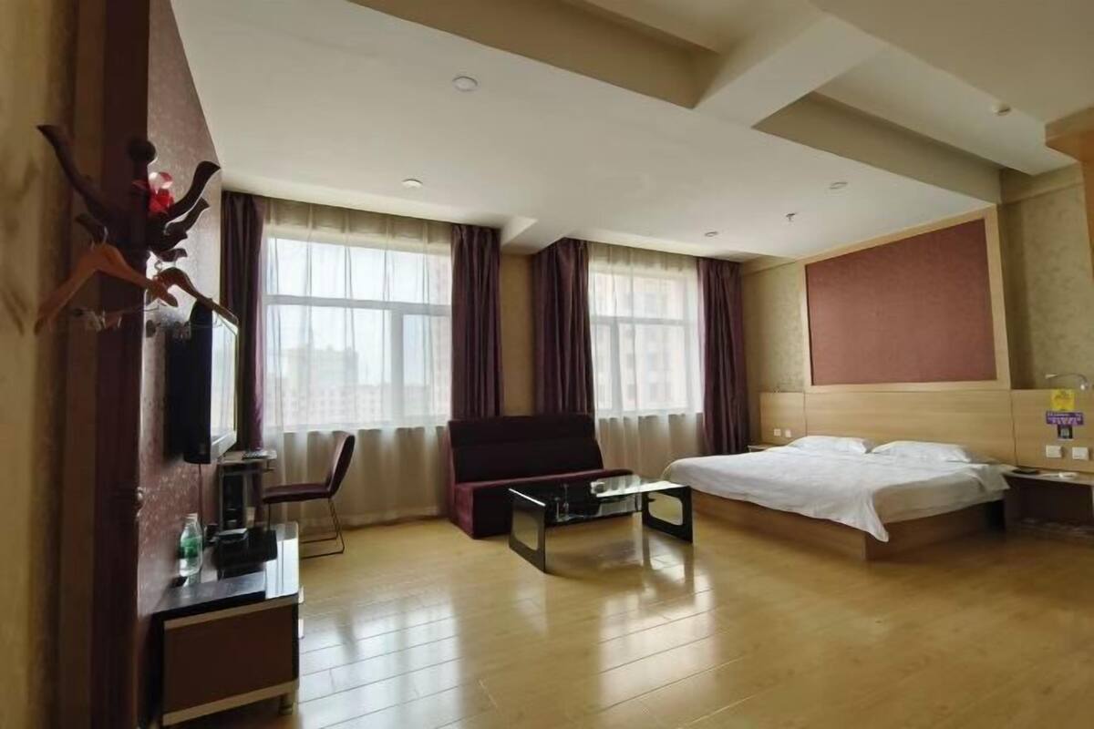 Ein Hotelzimmer mit Bett, Schreibtisch, Stuhl, Fernseher und einem fenster mit Vorhängen.