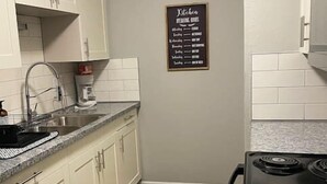 A compact kitchen with white cabinets, a granite countertop, a black stove, and a wooden floor. - The Mary Lou - Entire 2 Bedroom Apt in Quilt Town, USA (Hamilton)