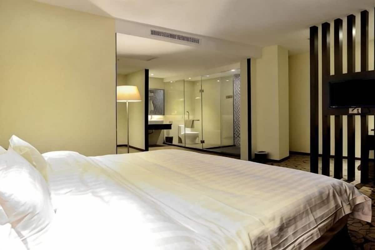 A hotel room with a bed, a mirror, a television, and a bathroom visible through an open door.