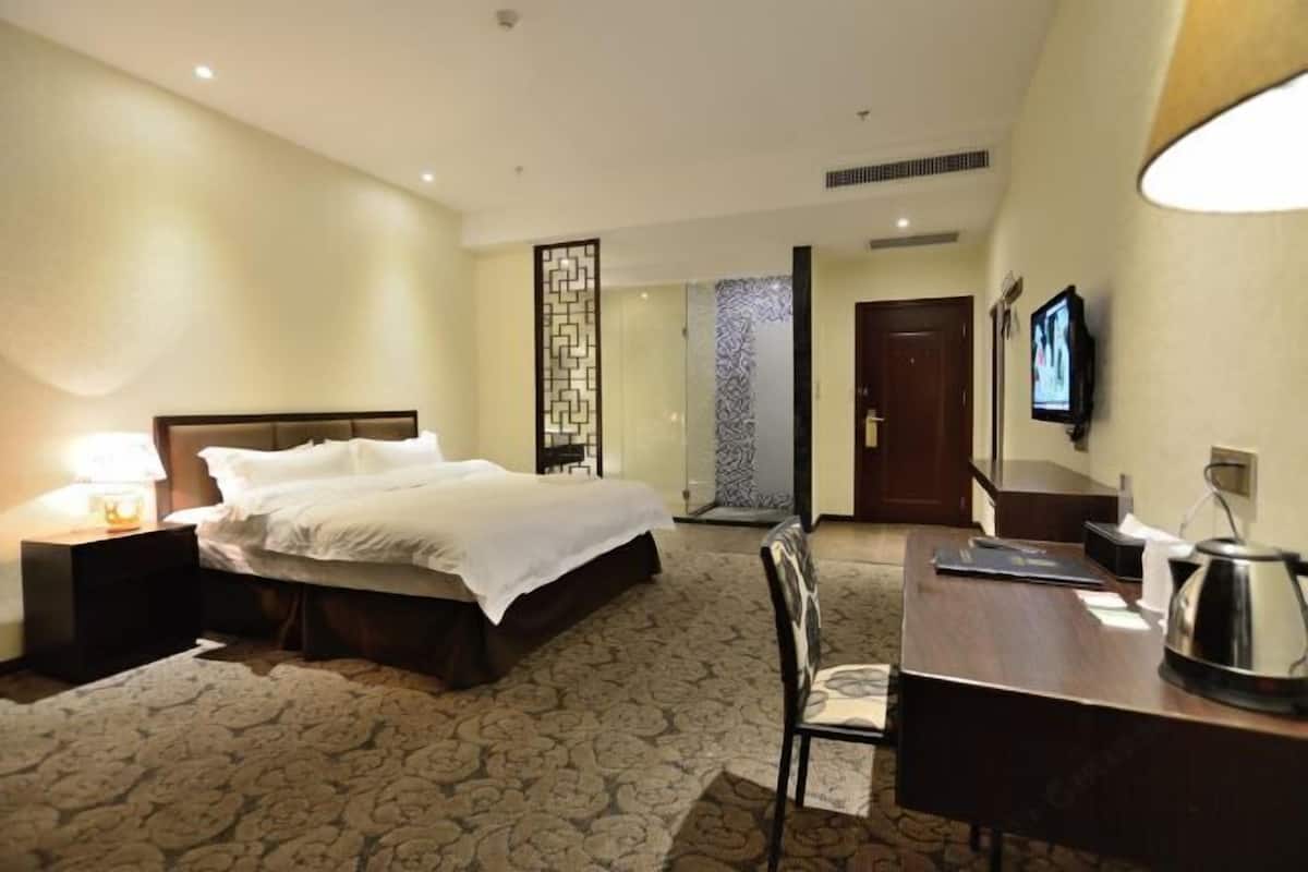 A hotel room with a bed, a desk, a chair, a TV, and a decorative screen.