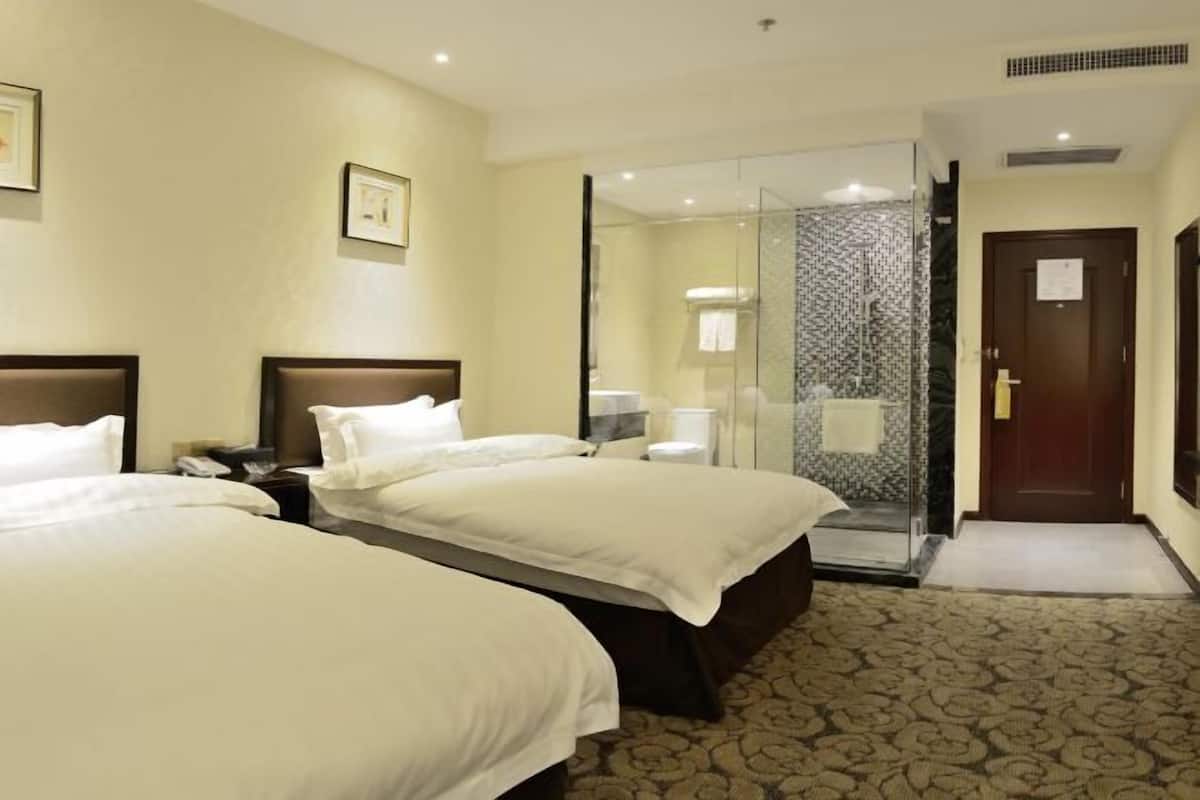 A hotel room with two beds, a glass shower enclosure, and a patterned carpet.