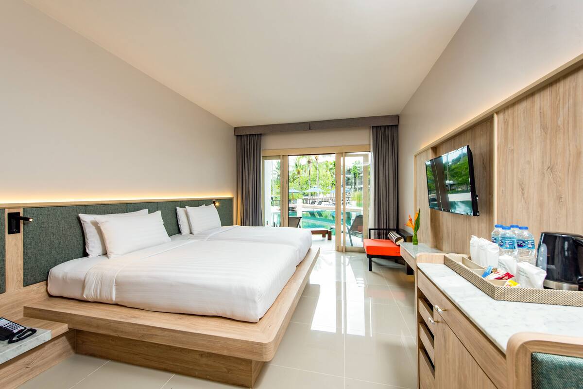 A hotel room with a large bed, a TV, a desk with a chair, and a view of the outdoors.
