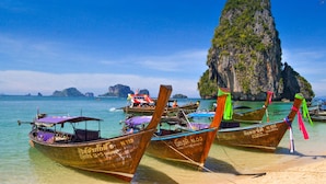 A beach with several traditional wooden boats tied to the shore, a clear blue sky, and a prominent rocky island in the background. - Holiday Ao Nang Beach Resort Krabi (Krabi)