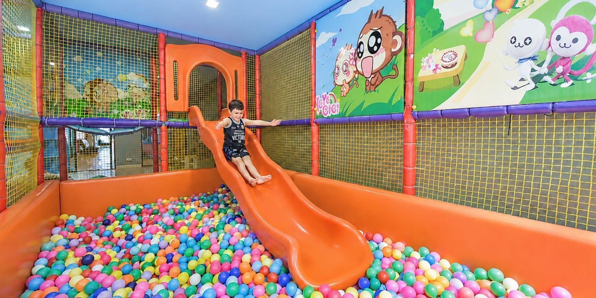 A child sliding down a colorful indoor slide into a ball pit filled with multicolored balls.