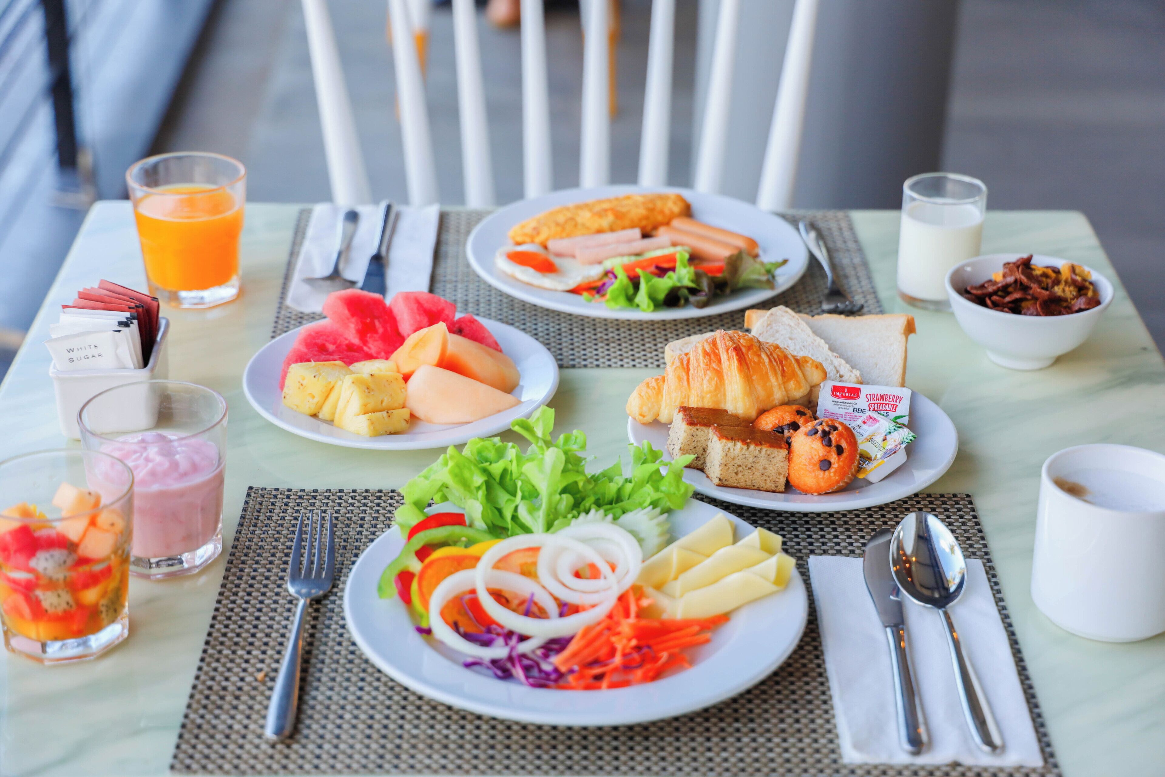 A table set with breakfast items including toast, eggs, and fruit, with a chair in the background.