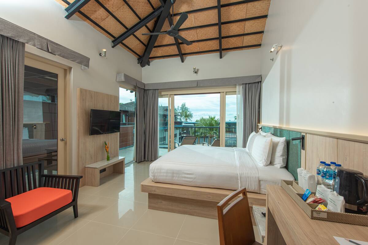 A modern hotel room with a large bed, a desk with amenities, a TV, and a balcony with a view.