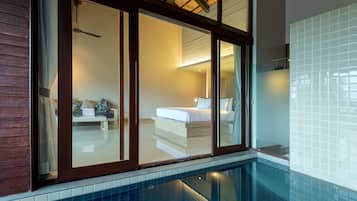 A modern hotel room with a large sliding glass door leading to a balcony, a neatly made bed, and a small seating area with a table and chairs.