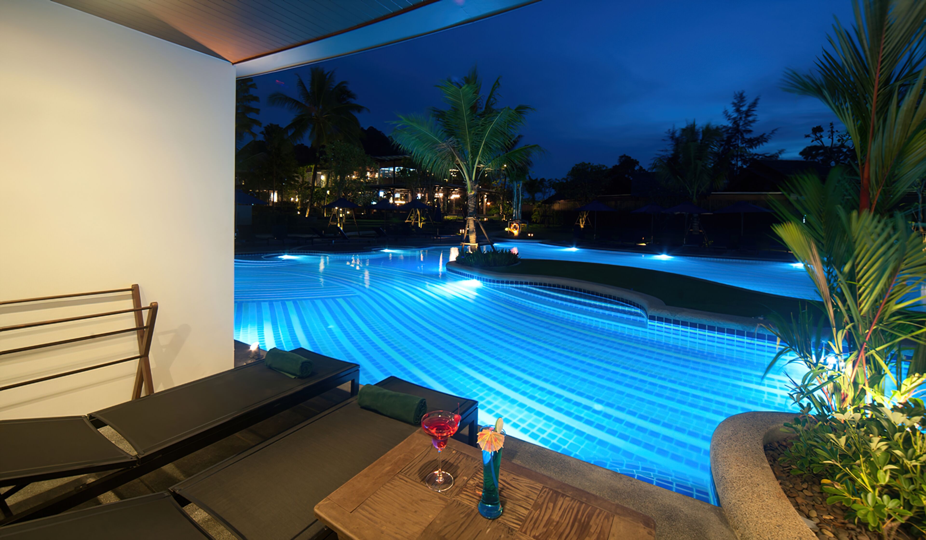 A pool with blue lighting, a table with a drink, and a chair.