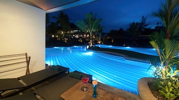 A pool with blue lighting, a table with a drink, and a chair.