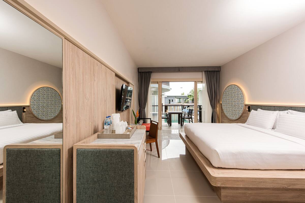 A modern hotel room with two beds, a desk with a tray of toiletries, a flat-screen TV, and a large mirror.