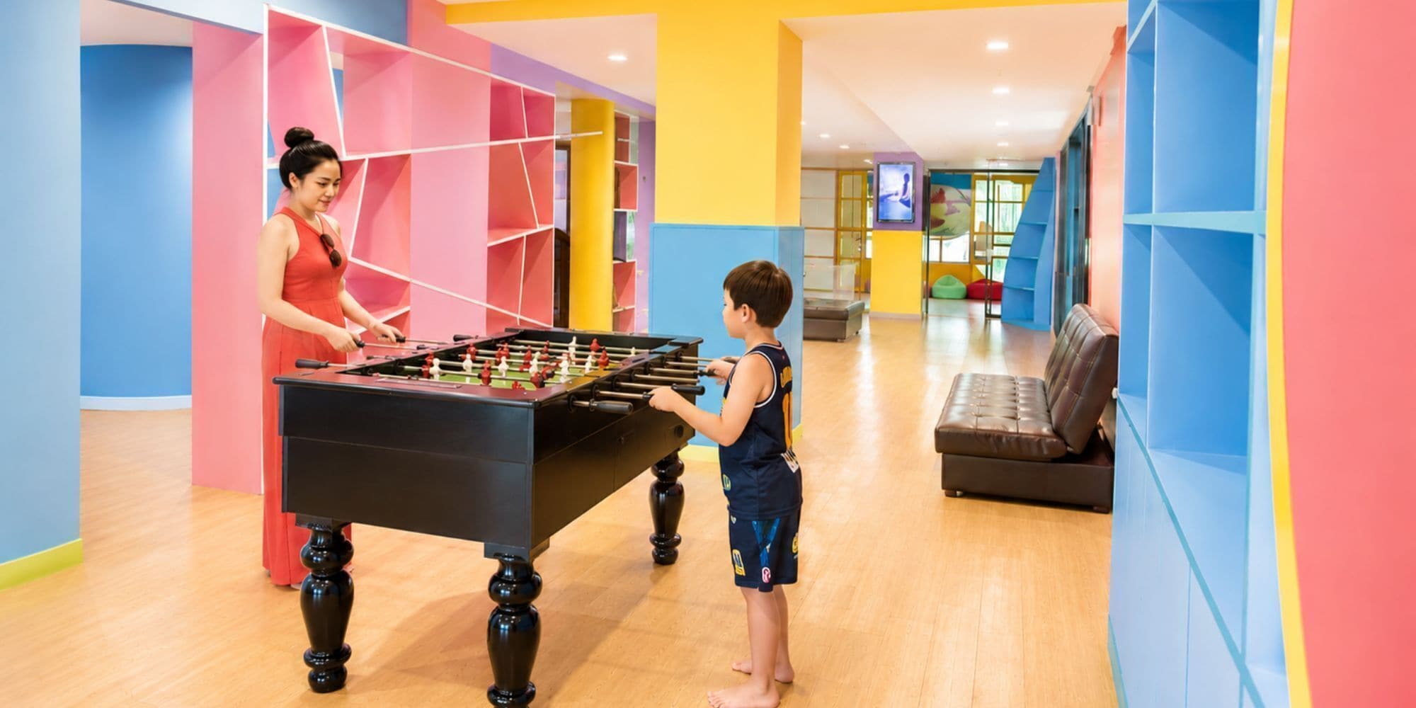 A room with a foosball table, a sofa, and colorful walls.