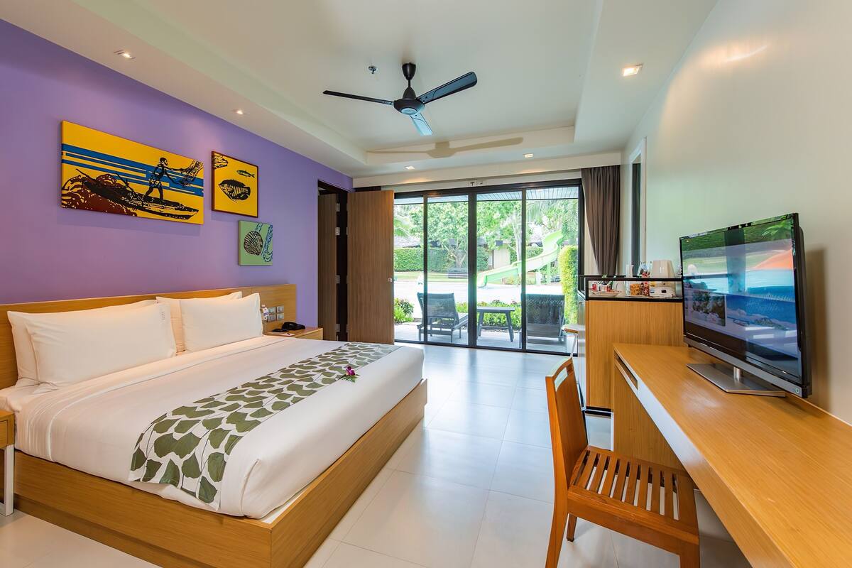 A hotel room with a bed, a desk with a TV, and a balcony with a view.