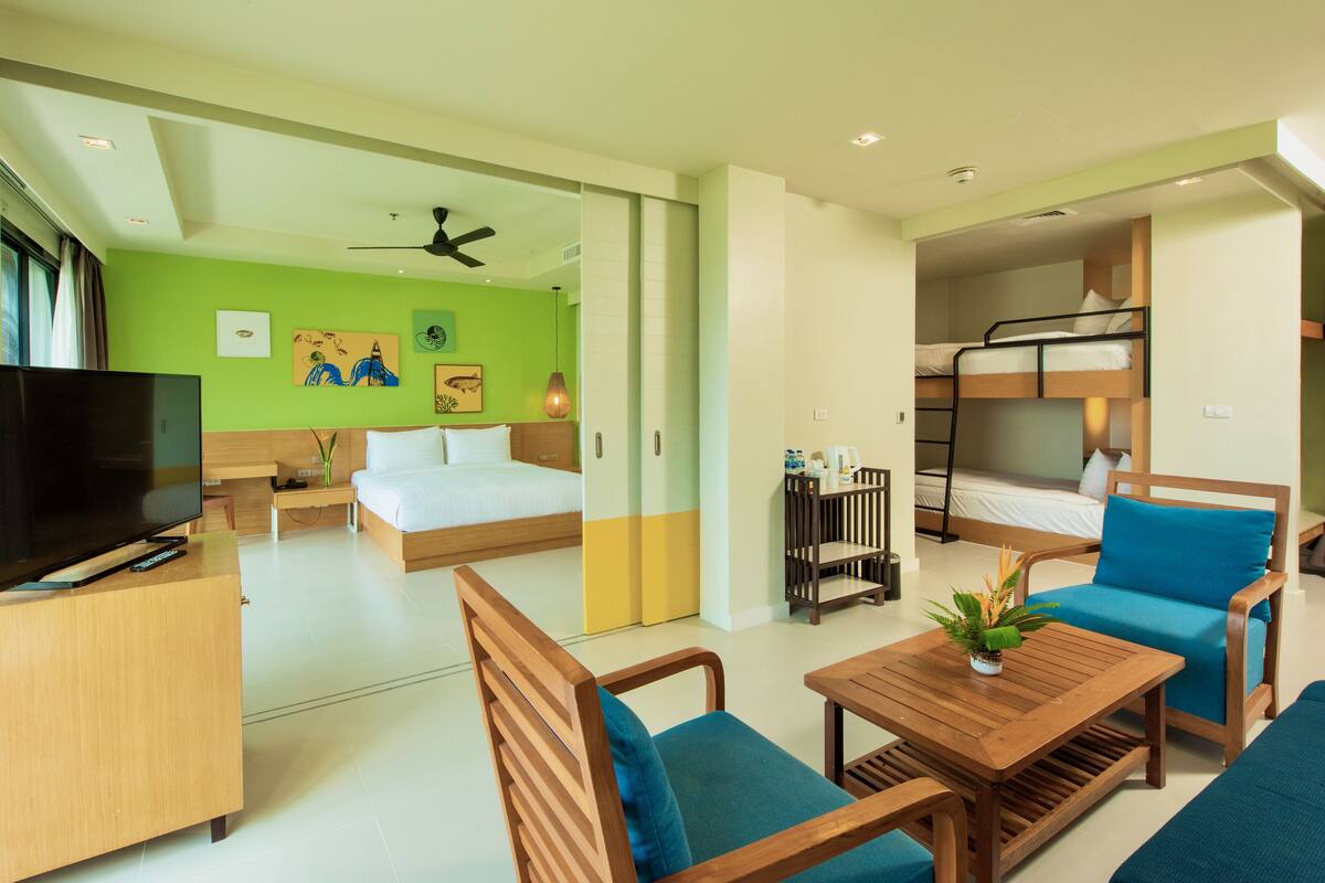 A modern hotel room with a bed, a TV, a desk, and a seating area with a table and chairs.