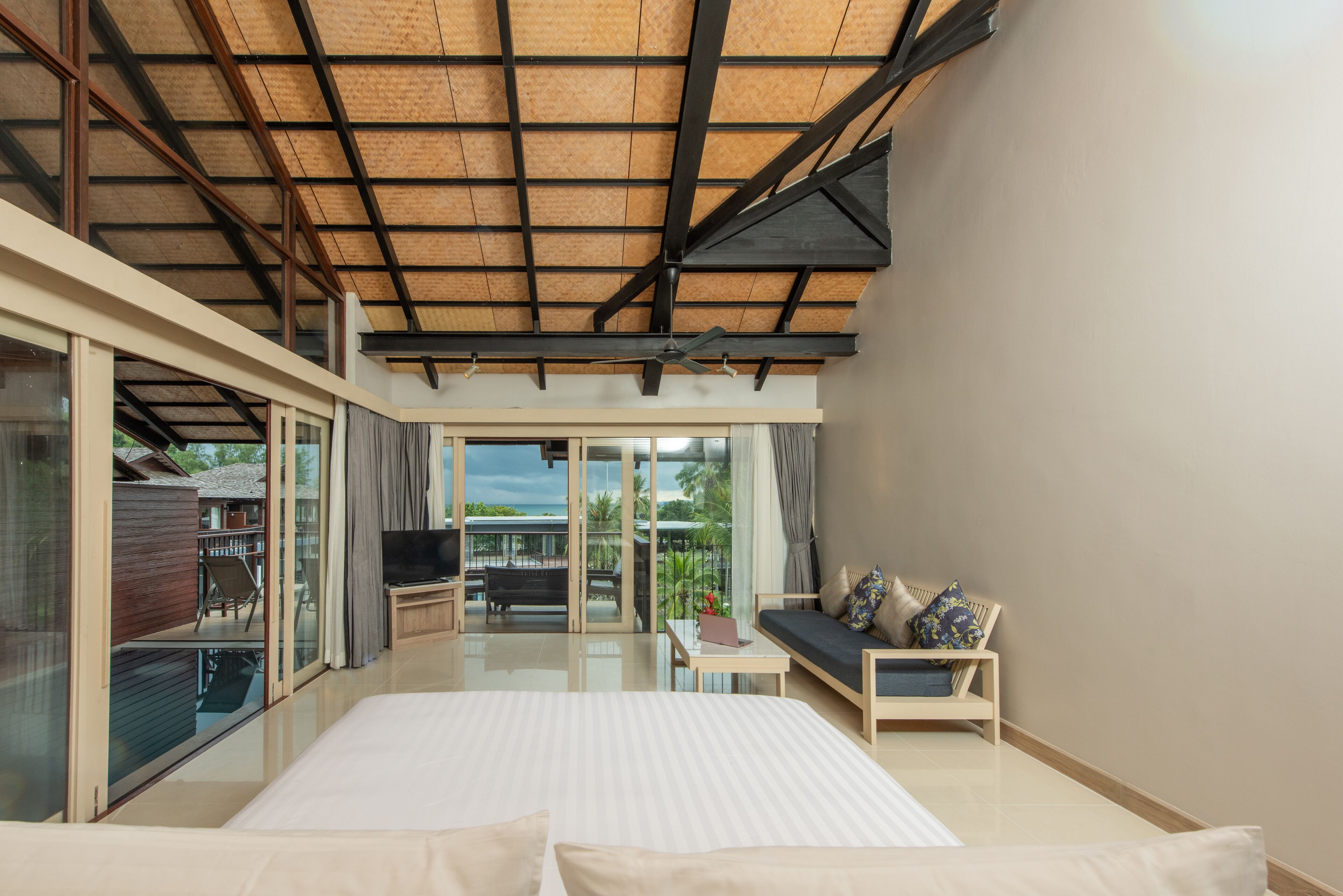 A spacious bedroom with a large bed, a seating area with a sofa and armchairs, and a balcony with a view of the surrounding area.