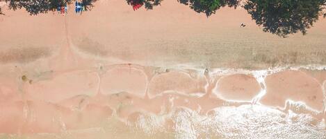 An aerial view of a beach with several boats anchored near the shore, surrounded by clear turquoise water and sandy beach.