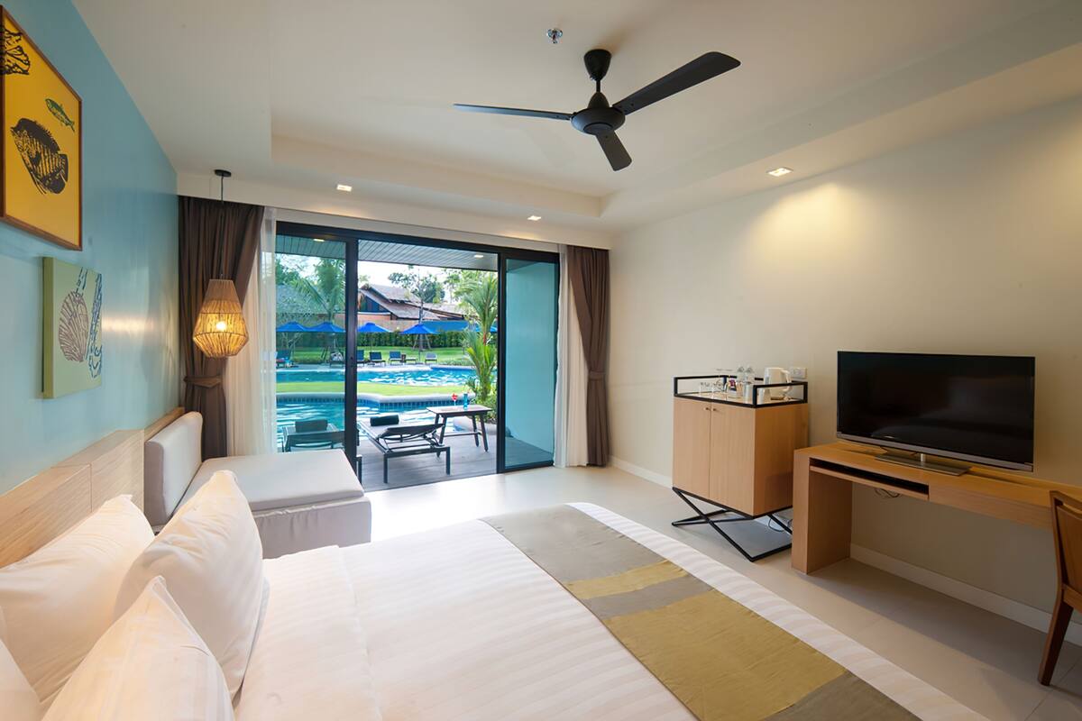 A hotel room with a bed, a TV, a desk, and a view of a pool and outdoor area.