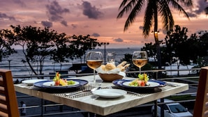 A table set for two with plates of food, glasses of wine, and a basket of bread, overlooking a beach with palm trees and a sunset. - Holiday Ao Nang Beach Resort Krabi (Krabi)