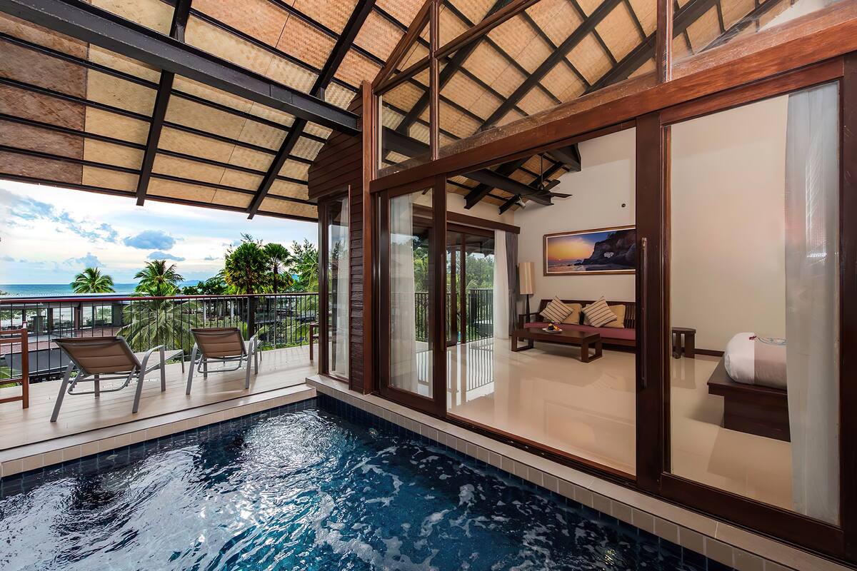 A swimming pool with lounge chairs, a balcony with a view of the ocean, and a room with a bed and a painting.