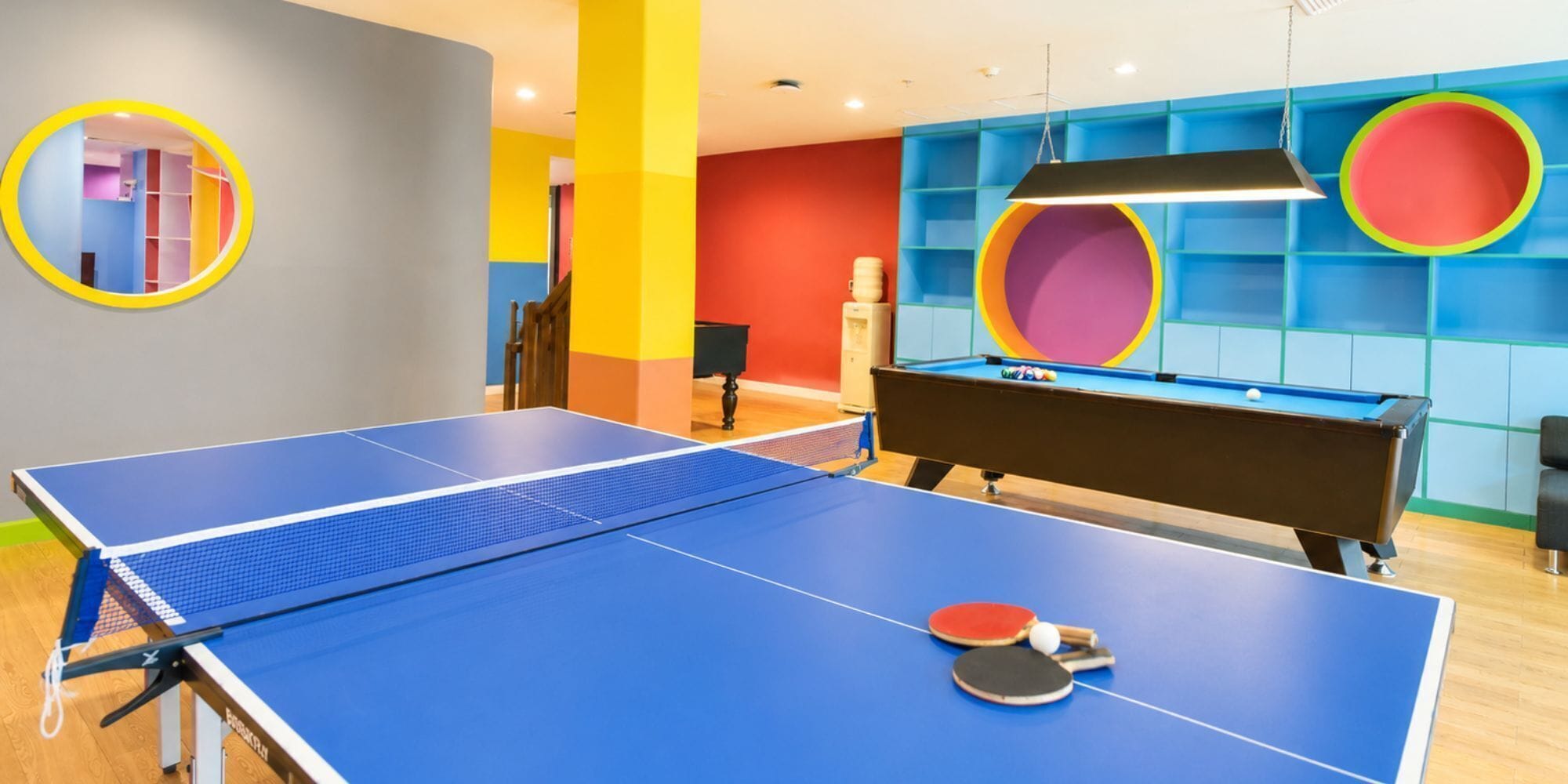A room with a blue ping pong table, a pool table, and colorful walls.