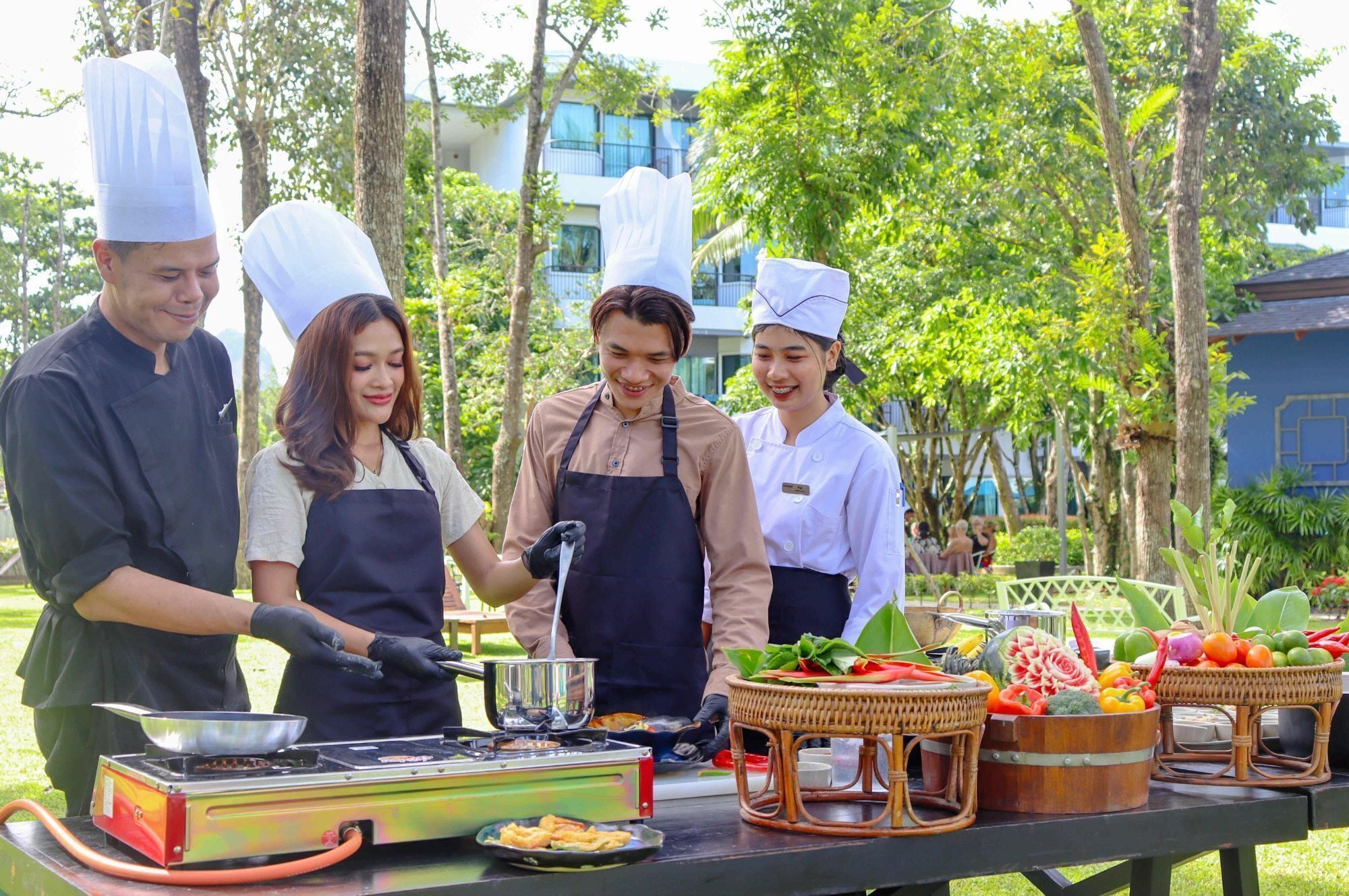 A group of chefs preparing food outdoors with a grill and baskets of fresh vegetables.