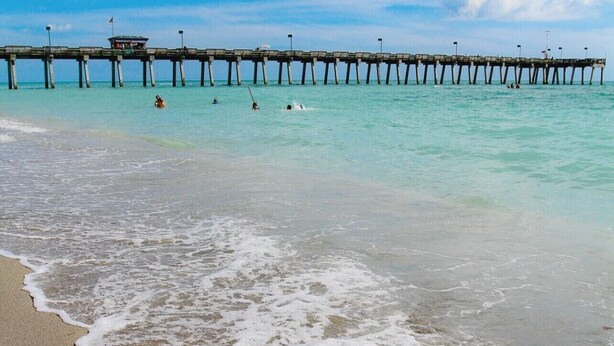 A beach with a wooden pier extending into the ocean, a lifeguard tower, and people swimming. - Lovely apartment 5 minutes to the beach, restaurants, shopping and services  (Venice)