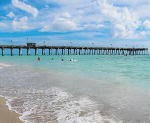 A beach with a wooden pier extending into the ocean, a lifeguard tower, and people swimming. - Lovely apartment 5 minutes to the beach, restaurants, shopping and services  (Venice)