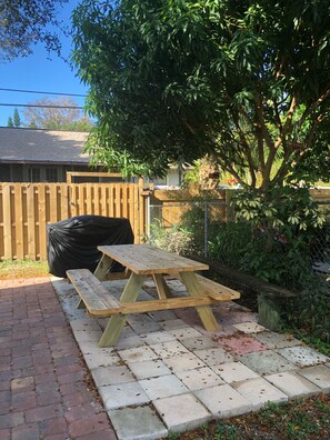 A picnic table set on a brick patio with a wooden fence and greenery in the background. - Lovely apartment 5 minutes to the beach, restaurants, shopping and services  (Venice)