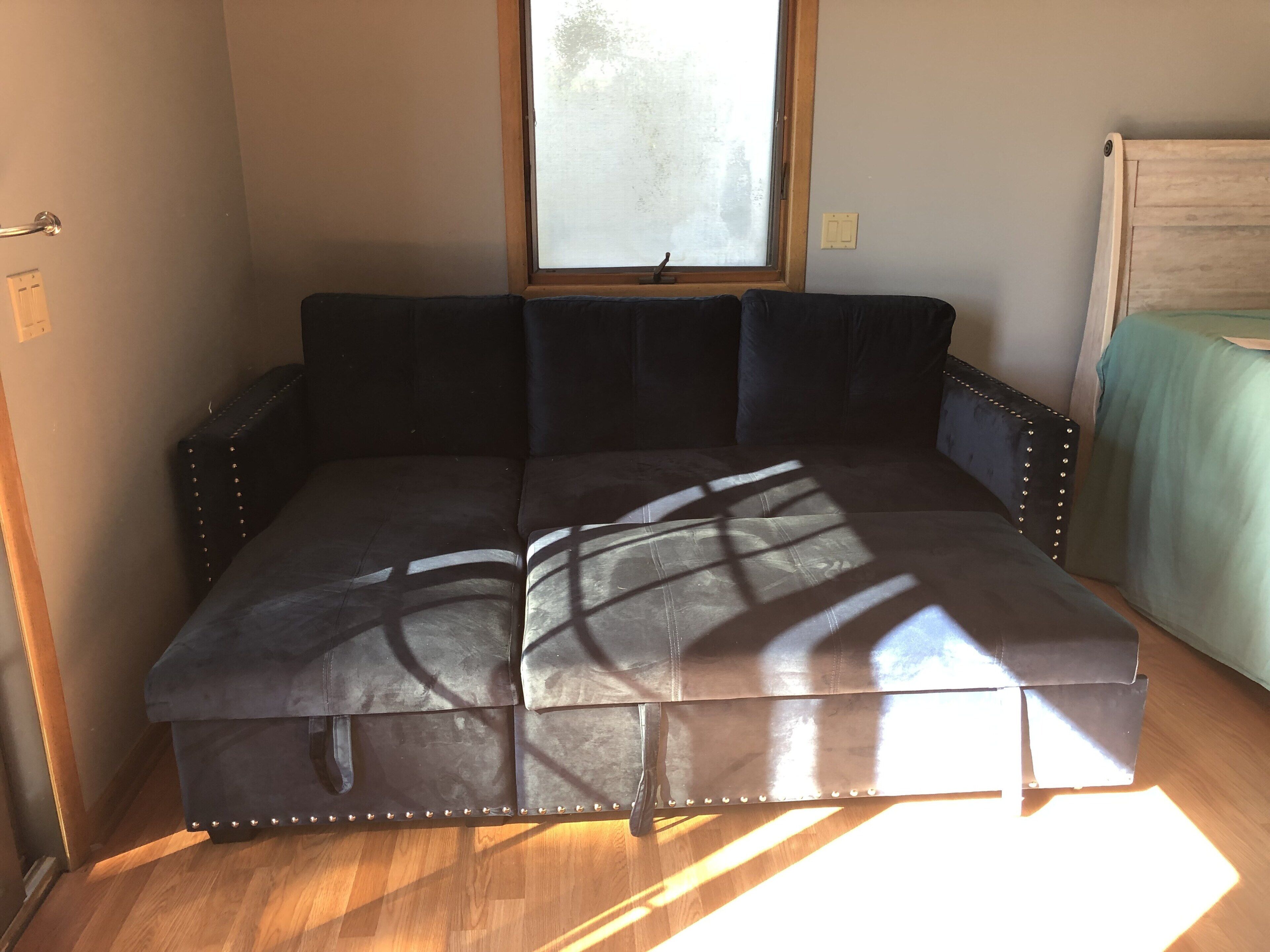 A dark-colored sofa with metal studs, positioned in a room with a wooden floor and a window.