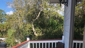 A balcony with wicker chairs and a potted plant, white railings, and a view of trees and foliage. - Lovely apartment 5 minutes to the beach, restaurants, shopping and services  (Venice)