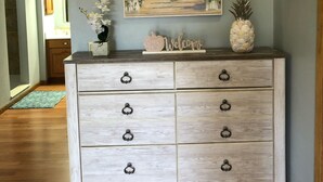 A wooden dresser with drawers and a painting of a coastal scene above it. - Lovely apartment 5 minutes to the beach, restaurants, shopping and services  (Venice)