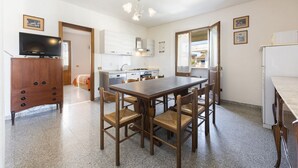 Eine moderne Küche mit weißen Schränken, einem Esstisch mit Stühlen, einem Fernseher auf einer Holzkommode und einem Kühlschrank.