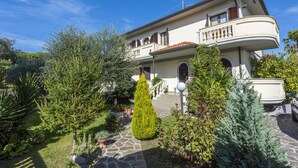 Ein zweistöckiges Haus mit Balkon, Steinweg und verschiedenen Pflanzen.