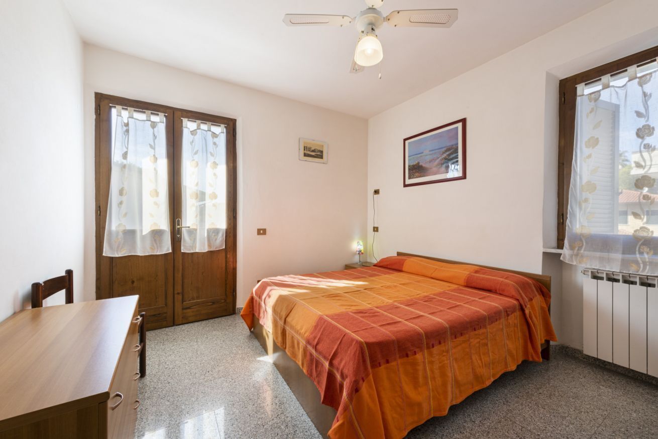 Ein Schlafzimmer mit Bett, Holzschreibtisch, Stuhl, Deckenventilator und einem Fenster mit Vorhängen.