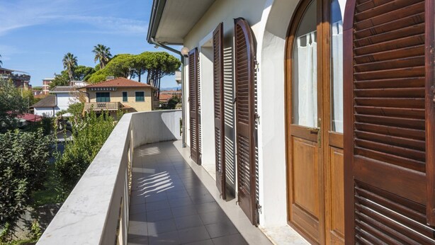 Ein Balkon mit Blick auf benachbarte Häuser, eine Tür mit Fenster und ein Fliesenboden.