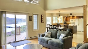 A spacious living room with a gray sofa, a round coffee table, and a view of a deck and lake. - Lakefront Escape - Private Dock - Pet Friendly (Albrightsville)