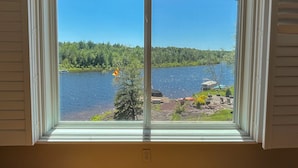 A window with a view of a lake, surrounded by greenery and a dock with boats. - Lakefront Escape - Private Dock - Pet Friendly (Albrightsville)