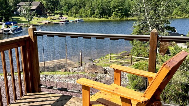 A wooden deck with a chair and a view of a lake with boats and houses in the background. - Lakefront Escape - Private Dock - Pet Friendly (Albrightsville)