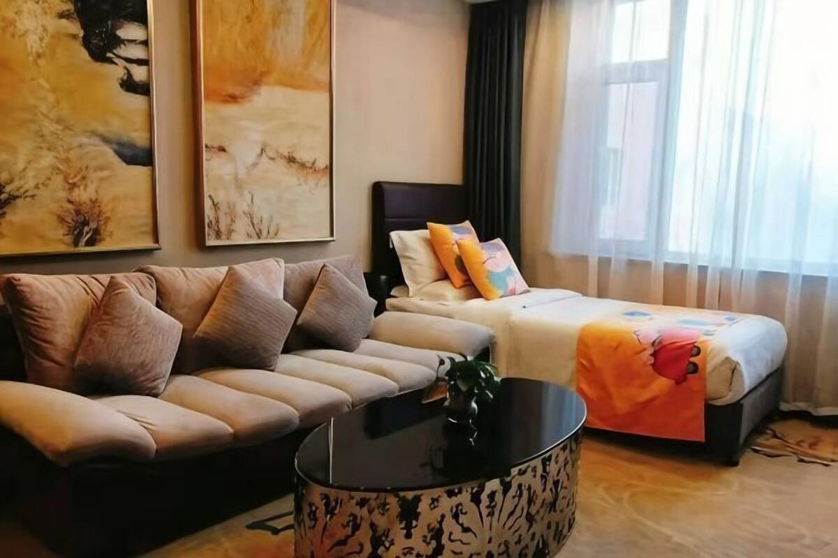 A hotel room with a sofa, a bed, a round coffee table, and artwork on the walls.