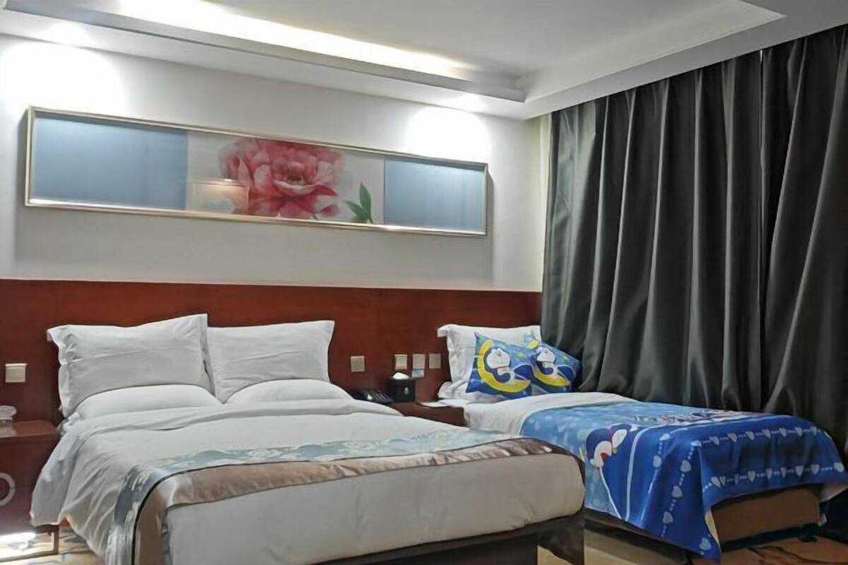 A hotel room with a large bed, a smaller bed, a nightstand, a lamp, a painting, and a window with curtains.