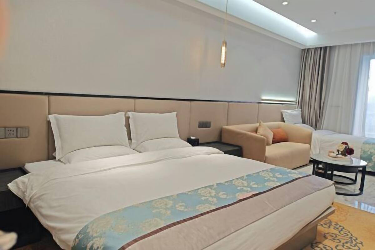 A hotel room with a large bed, a sofa, a small table, and a view of the outdoors.