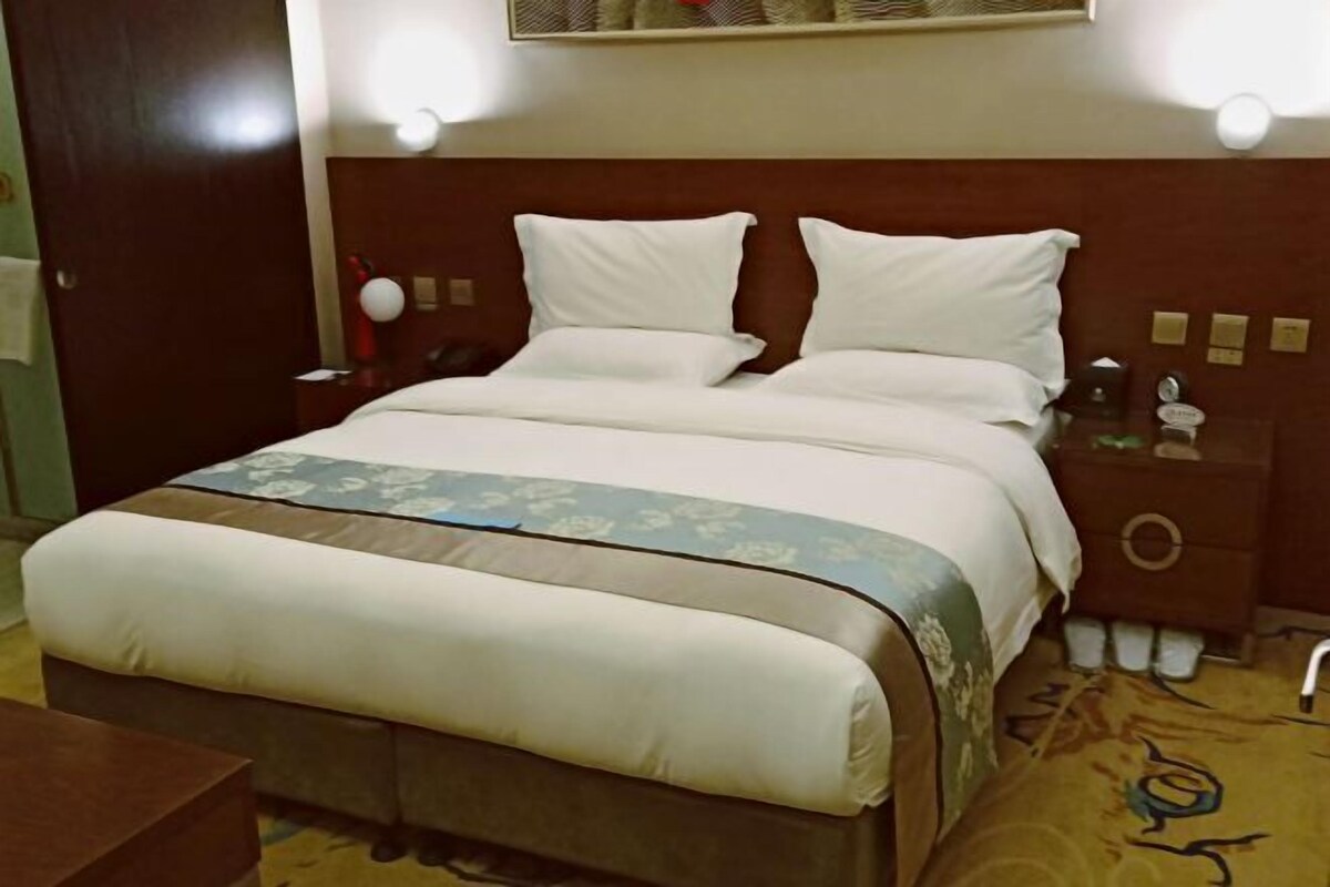 A hotel room with a large bed, a nightstand, a dresser, and a carpeted floor.