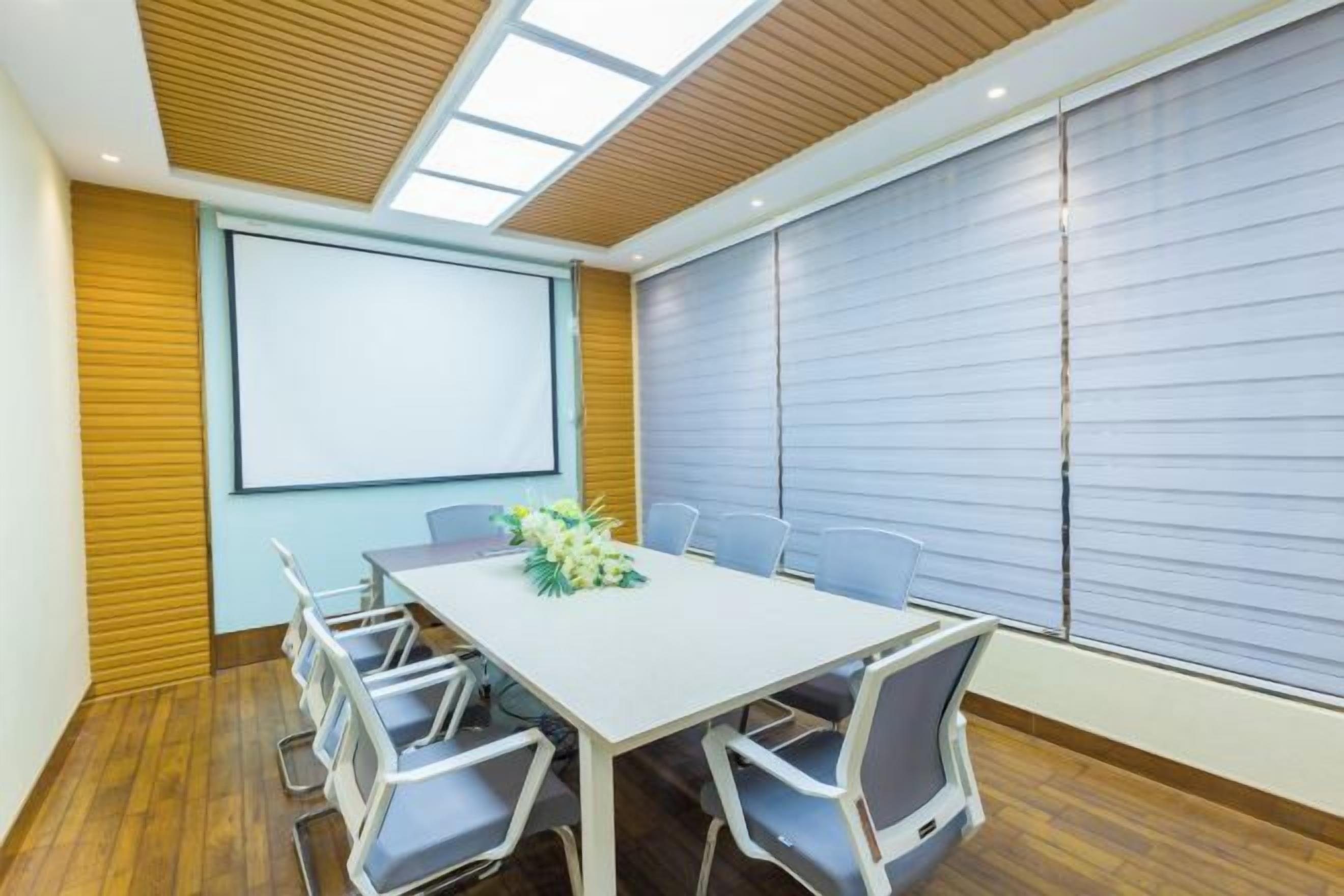 A conference room with a white table, six chairs, a projector screen, and a large window with blinds.