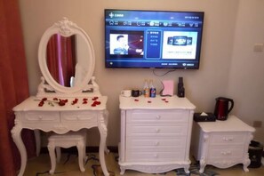 A room with a television mounted on the wall, a white vanity with a mirror, and two white dressers. - JT Days Hotel (Changchun)