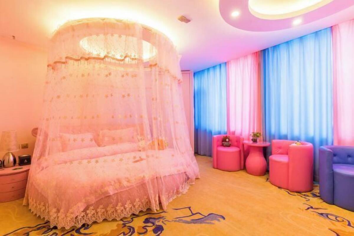 A room with a canopy bed, pink and blue curtains, and a round table with a chair.