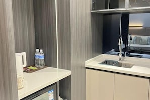 A modern kitchen with a white countertop, a sink, and a cabinet. There are two bottles of water and a coffee maker on the counter.
