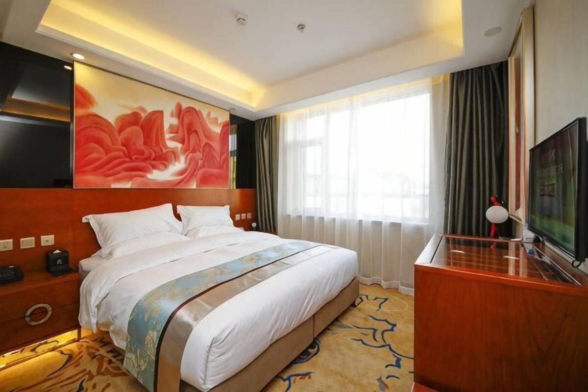 A hotel room with a large bed, a TV, a desk, and a painting on the wall.